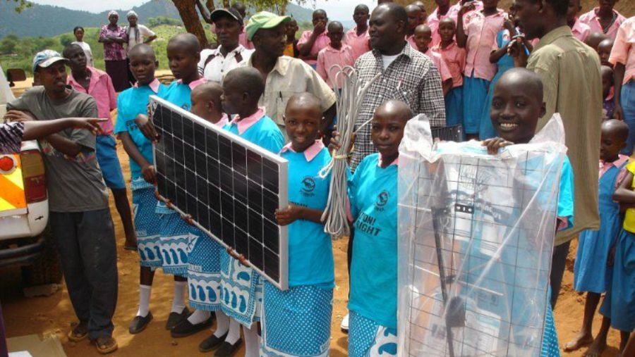 Unas niñas sostienen unos paneles solares en Kamaindi