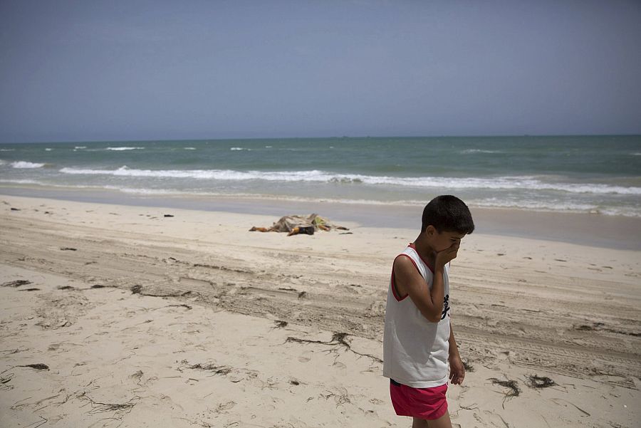 Un niño camina junto a los cuerpos sin vida de migrantes que han aparecido en una playa de Libia.