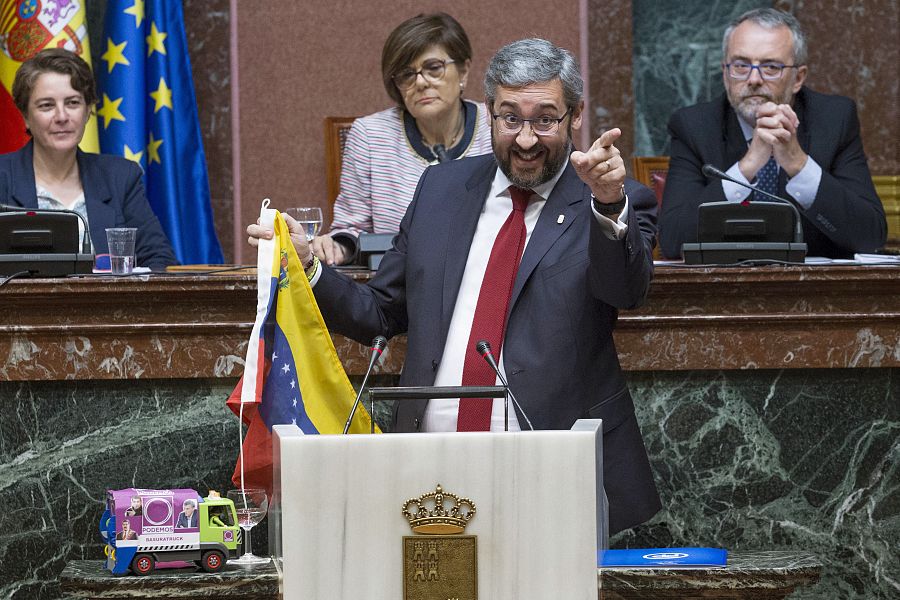 El portavoz del PP muestra una bandera de Venezuela y un camión de la basura con fotos del secretario general de Podemos en Murcia