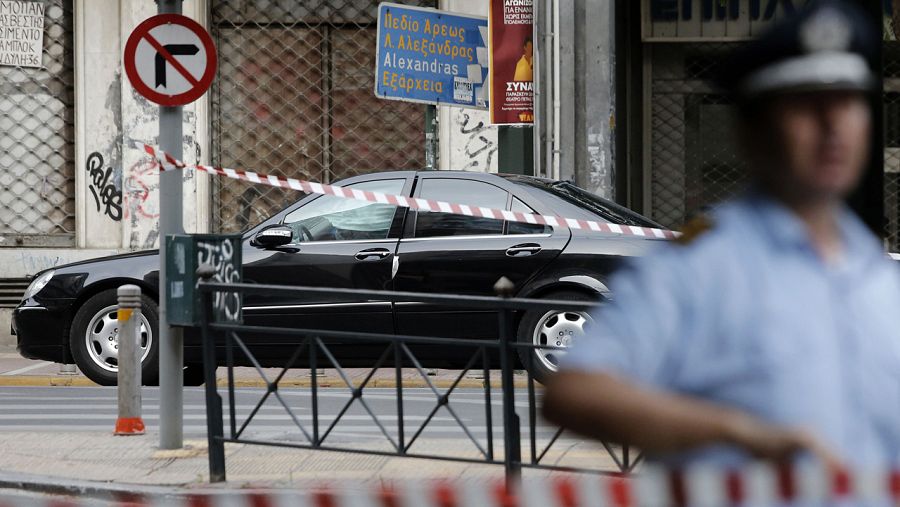 Un policía vigila el area acordonada con el coche del ex primer ministro Papadimos, tras la explosión