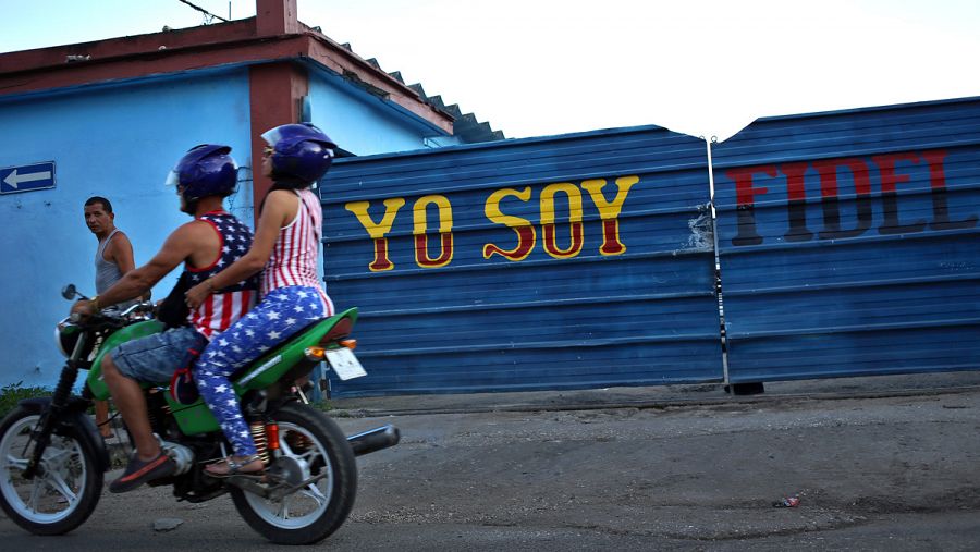 Una pareja en motocicleta cruza frente a un letrero en honor a Fidel Castro en La Habana