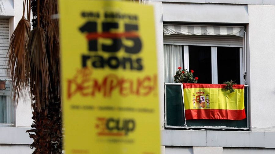 Una bandera española de fondo junto a un cartel contra el 155