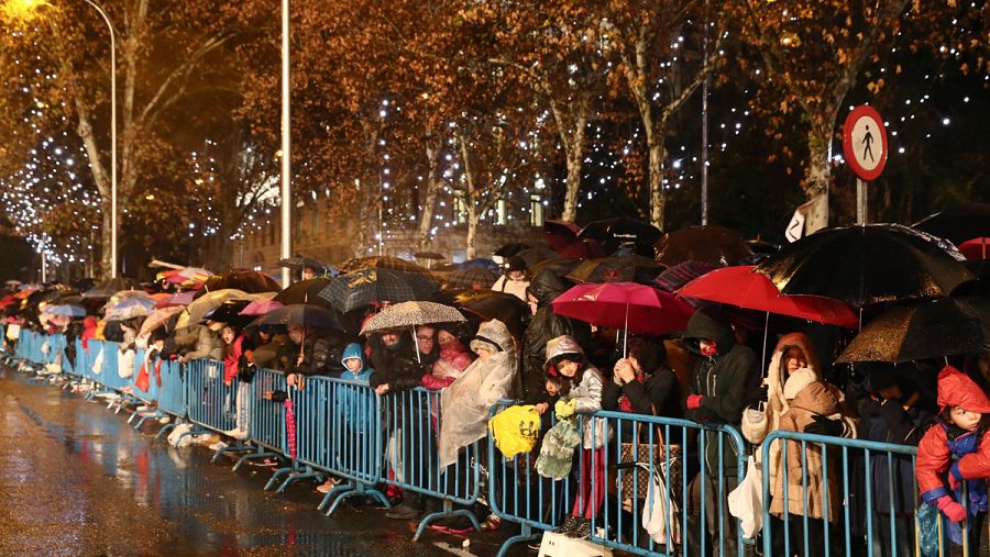 Miles de niños aguardan refugiados bajo los paraguas a la llegada de los Reyes Magos en la madrileña plaza de Cibeles