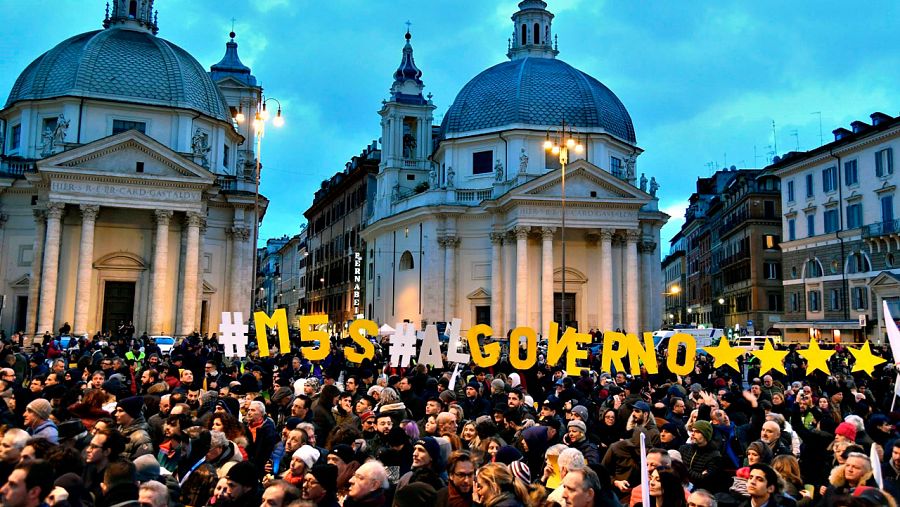 Los simpatizantes del Movimiento Cinco Estrellas asisten al acto de cierre de campaña de las elecciones generales en Roma, con un mensaje que reza: 