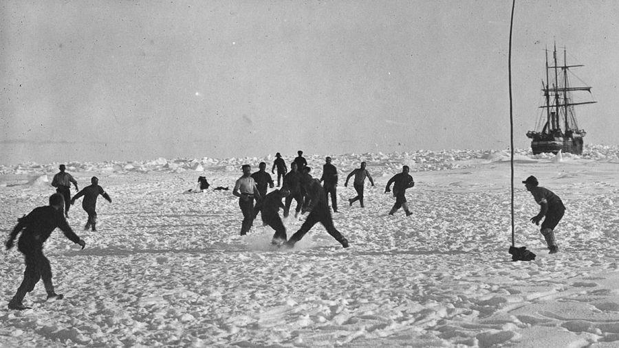 Los miembros de la Expedición Imperial Transantártica, jugando al fútbol en la nieve, con el Endurance de fondo.