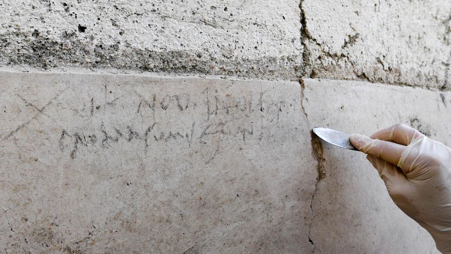 Una arqueóloga señala la inscripción de una pared encontrada en una excavación en Pompeya, Nápoles.