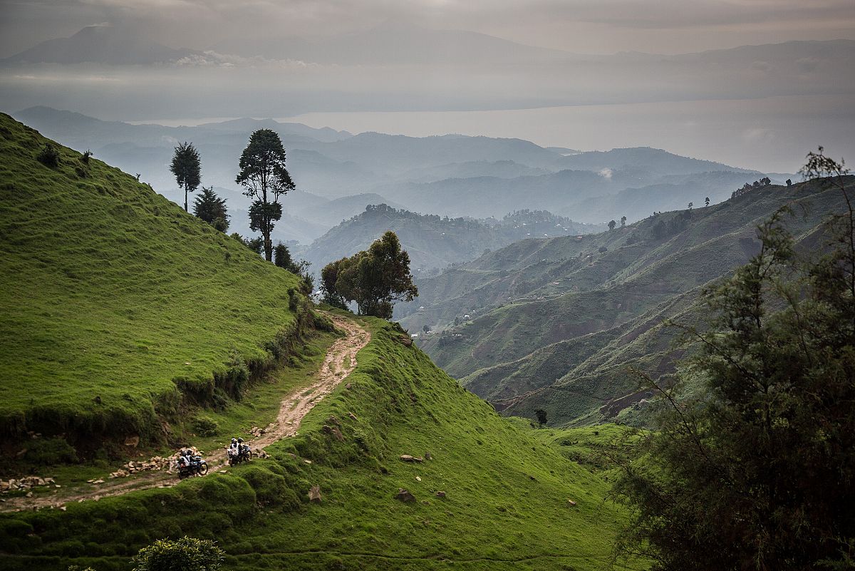 Unos motoristas avanzan por un camino en la ladera de una montaa cubierta de vegetacin, camino de Numbi.