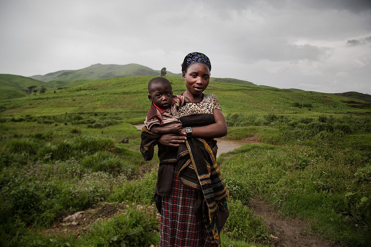 Asefili, una trabajadora del coltán, mira a cámara con su hijo en brazos en medio del campo.
