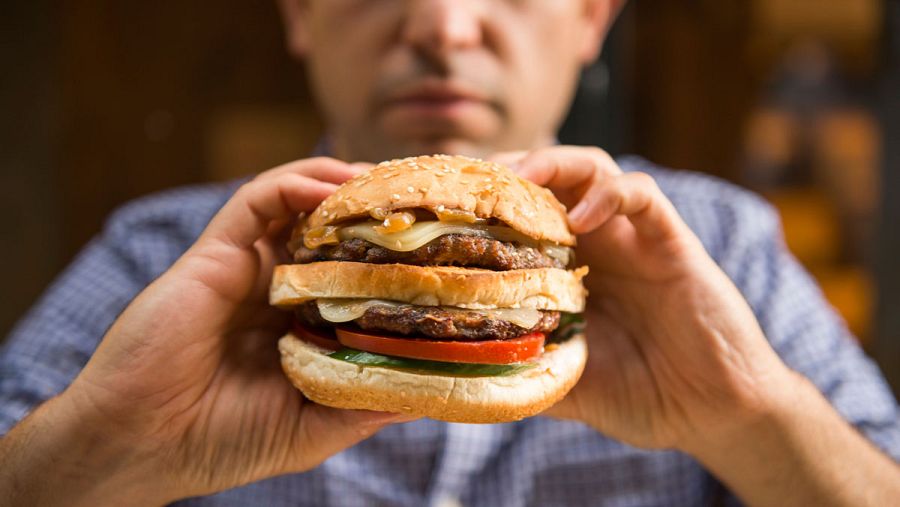 Un hombre sujeta una hamburguesa con ambas manos