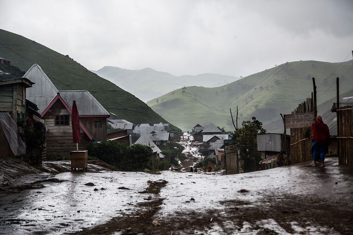 Imagen de Numbi lloviendo, vista desde lo alto de su calle principal. Varias figuras caminan por la brillante y mojada pista de tierra.