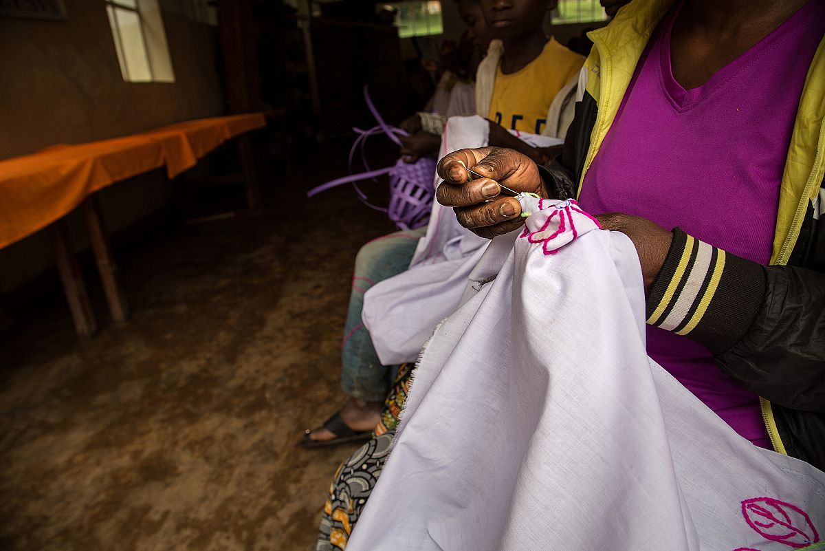 Primer plano de las manos de una de las pacientes de Panzi, bordando una tela. Detrás se adivinan otras mujeres haciendo la misma tarea.