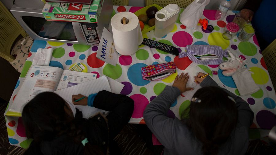 Manos de niños estudiando en una mesa de casa.