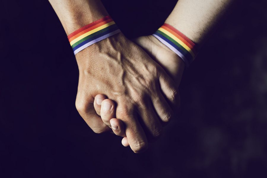 Las manos de dos personas agarradas y con pulseras de arcoíris en representación de la bandera LGTBI.