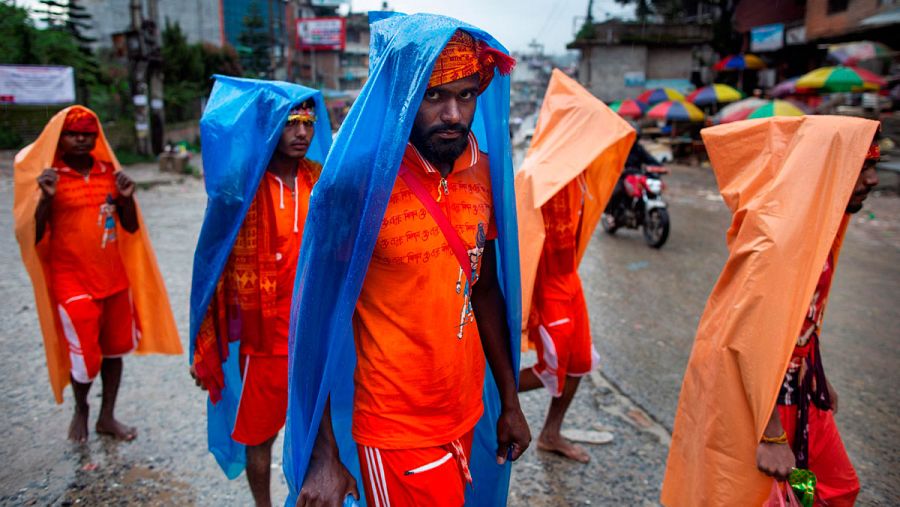 Un grupo de peregrinos ataviados de naranja se cubre la cabeza para protegerse de la lluvia durante la caminata.