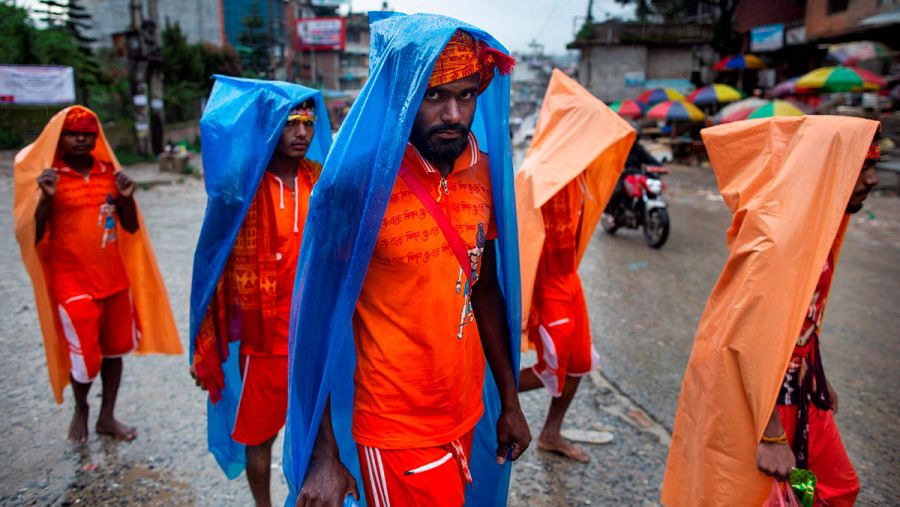 Un grupo de peregrinos ataviados de naranja se cubre la cabeza para protegerse de la lluvia durante la caminata.