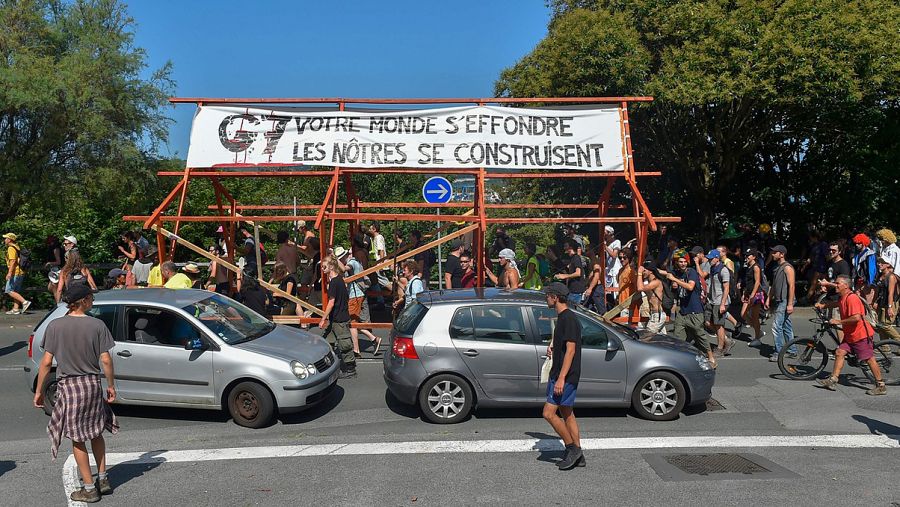 Manifestantes de la contracumbre del G7 recorren en Hendaya con una pancarta en la que se lee: 