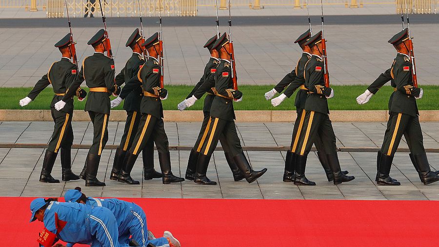 Trabajadores colocan la alfombra roja mientras un grupo de militares ensayan para el desfile conmemorativo del 70 aniversario de la República Popular China.