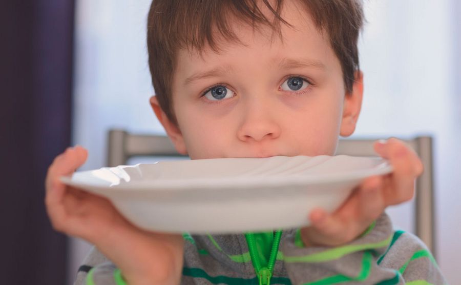 Un niño con ojos de súplica presenta un plato vacío pidiendo alimento.