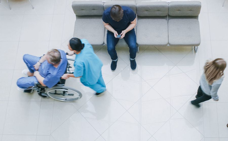 Una celadora lleva en silla de ruedas a un paciente.