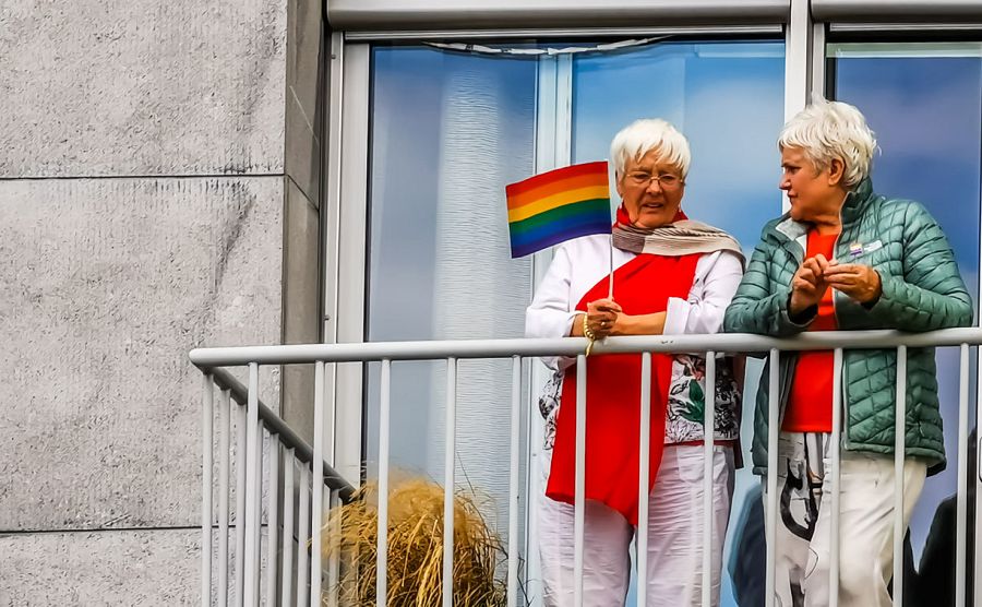 Dos mujeres mayores celebran el día del orgullo gay en un balcón con la bandera del arco iris.