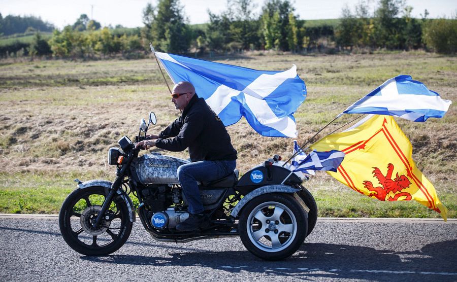 Un motociclista conduce con la bandera de Escocia y el Estandarte Real de Escocia, más conocida como el 