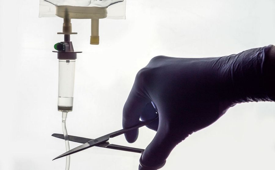 Las manos de un profesional sanitario cortan con unas tijeras una vía intravenosa.