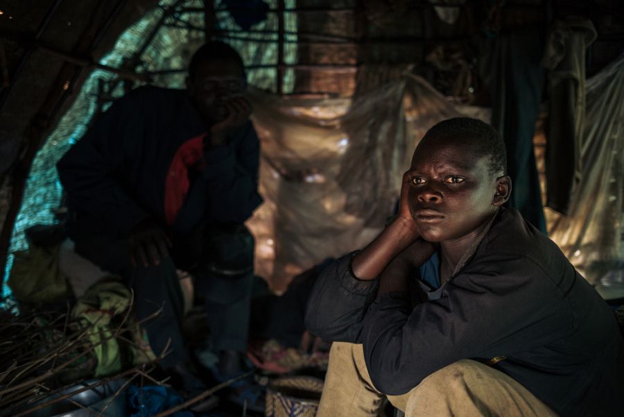 Benjamin, 16 años, sentado junto a su padre en su refugio de plástico en el campo de desplazados de Rho.