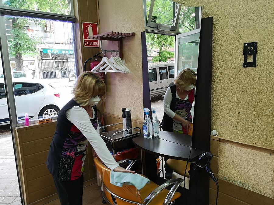 La dueña de una peluquería limpia uno de los sillones antes de abrir el local