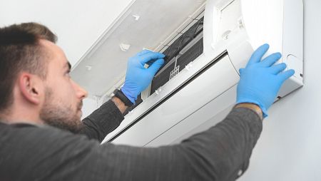 Una persona con guantes revisa un aparato doméstico de aire acondicionado.