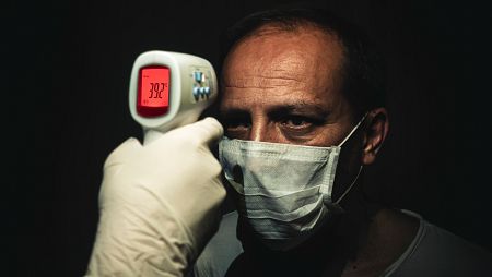 Toma de temperatura con un termómetro de rayos infrarrojos a un hombre con mascarilla sanitaria.