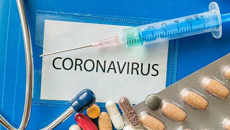 Jeringuilla sobre la palabra coronavirus escrita en un papel.