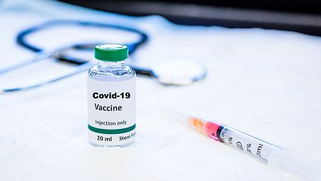 Jeringuilla junto a botecito de vacuna etiquetado con COVID-19.