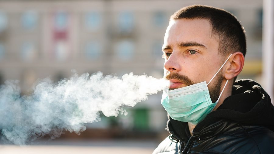 Joven fumando con mascarilla en la barbilla