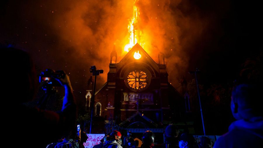 Un grupo de manifestantes observa como arde la iglesia de San Francisco de Borja, actualmente destinada al servicio religioso de Carabineros de Chile, este domingo durante una manifestación en los alrededores de la Plaza Italia de Santiago (Chile).