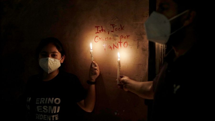 Una mujer sostiene una vela junto a los nombres de los dos fallecidos en las protestas