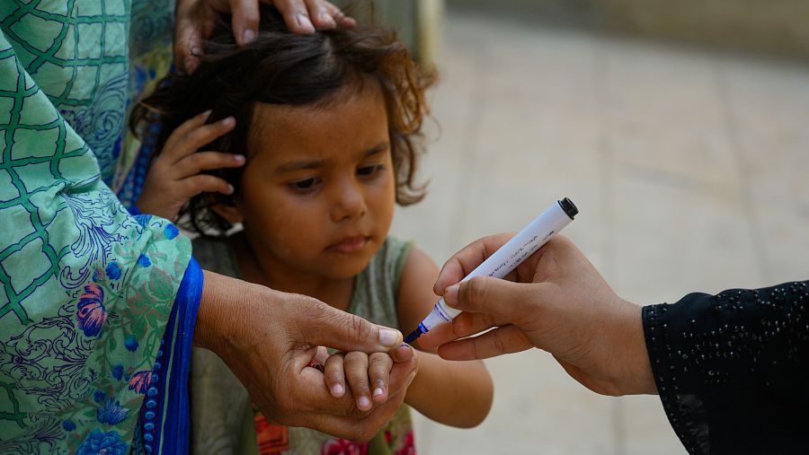 Una trabajadora sanitaria marca  con rotulador permanente el dedo de una niña de tres años a  la que acaba de vacunar contra la polio, en Pakistán.