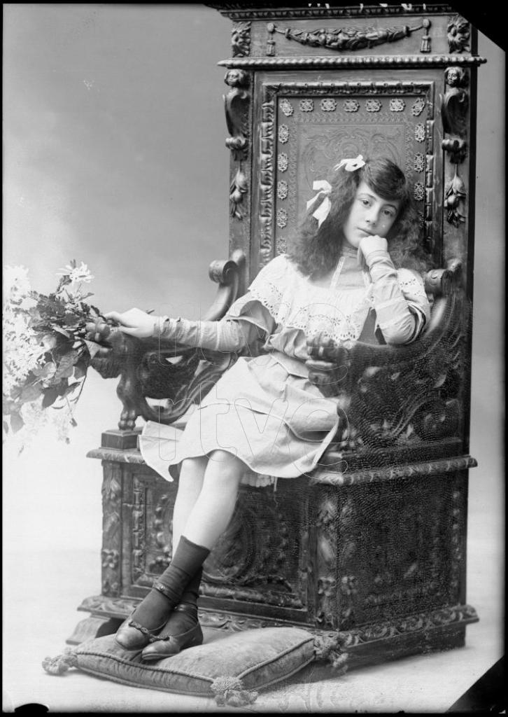 NIÑA CON UN RAMO, SENTADA EN UN SILLON DE MADERA LABRADA