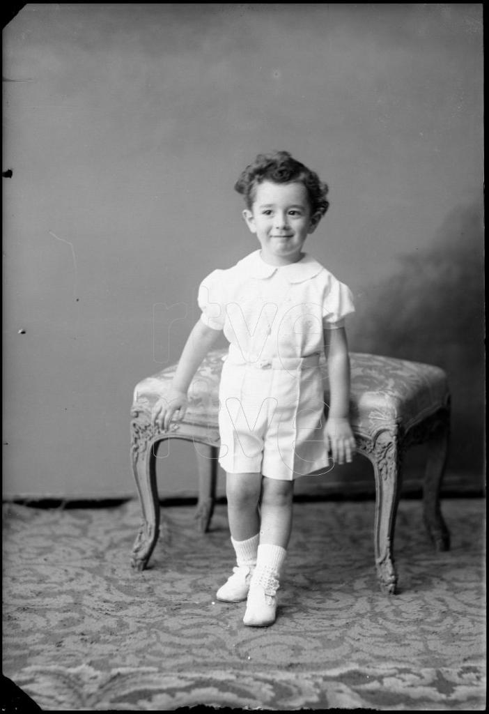 NIÑO DE CORTA EDAD APOYADO EN UN ESCABEL