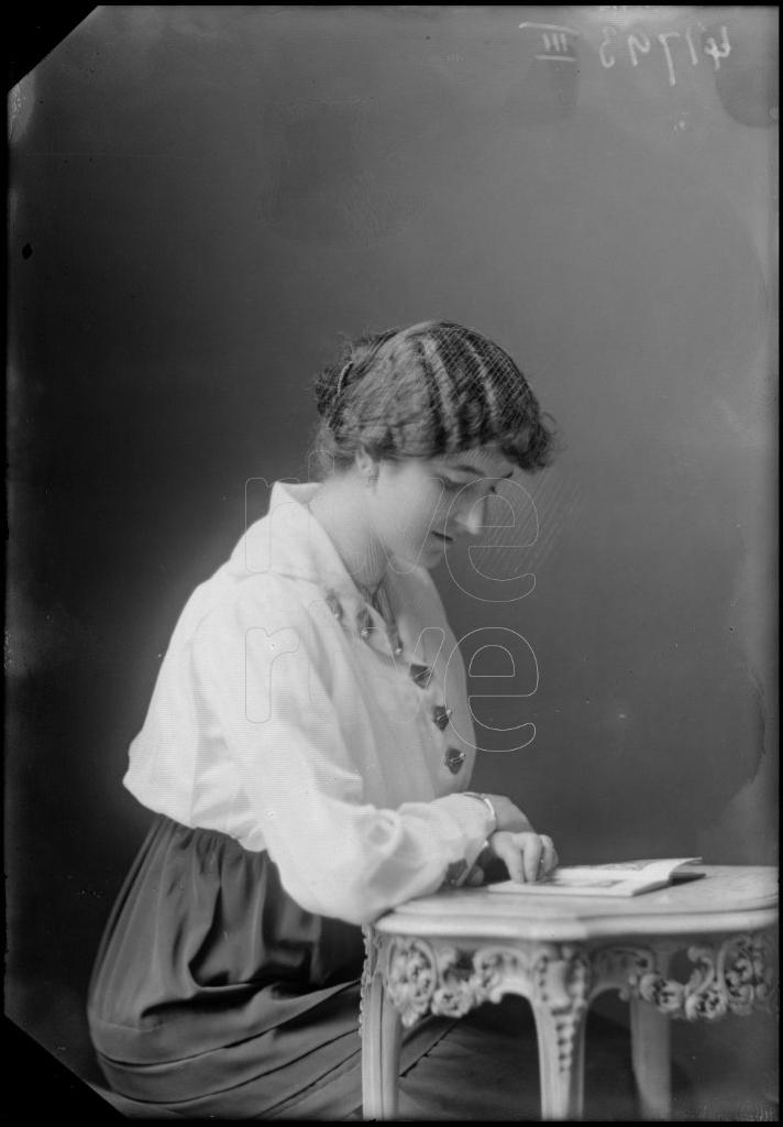 MUJER SENTADA LEYENDO UN LIBRO, APOYADA EN UNA MESA