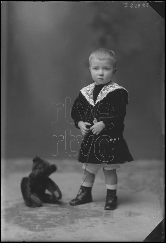 NIÑO DE CORTA EDAD DE PIE JUNTO A UN PELUCHE