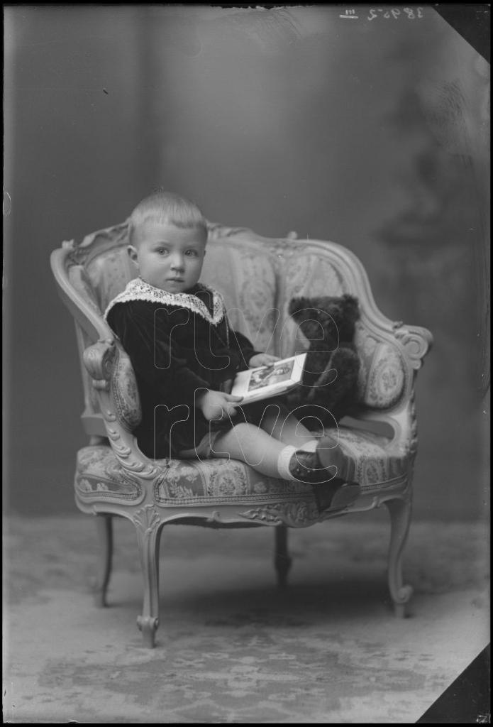 NIÑO DE CORTA EDAD CON UN LIBRO Y UN PELUCHE, SENTADO