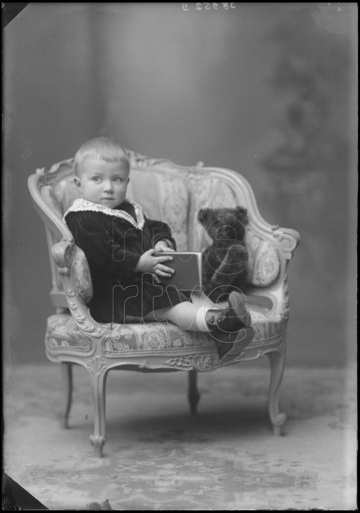 NIÑO DE CORTA EDAD CON UN LIBRO Y UN PELUCHE, SENTADO