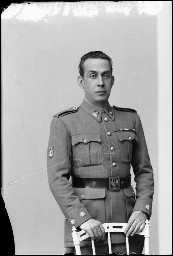 TENIENTE CORONEL, APOYADO EN EL RESPALDO DE UNA SILLA