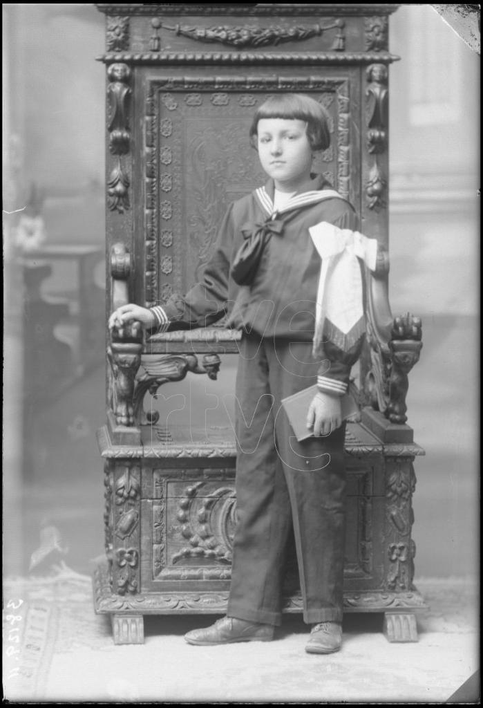 NI&Ntilde;O VESTIDO DE PRIMERA COMUNION, DE PIE JUNTO A UN SILLON D