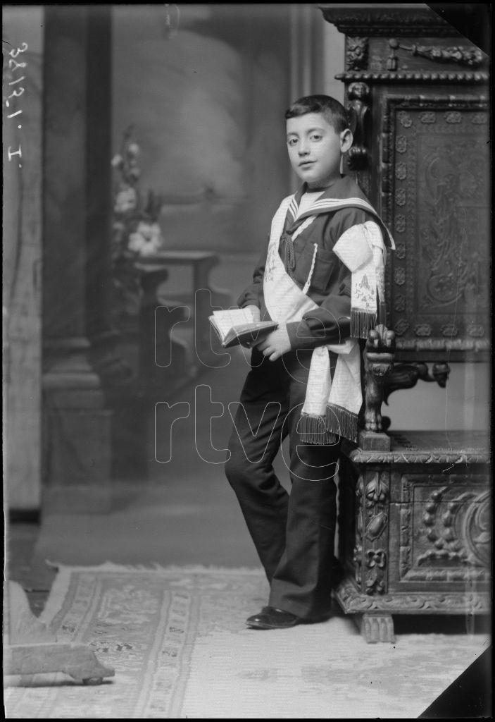 NIÑO VESTIDO DE PRIMERA COMUNION , APOYADO EN UN SILLON DE M