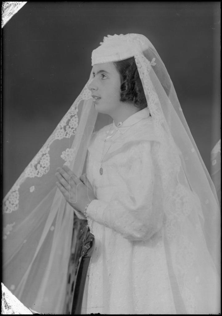 NI&Ntilde;A VESTIDA DE PRIMERA COMUNION, DE PERFIL JUNTO A UN RECLI