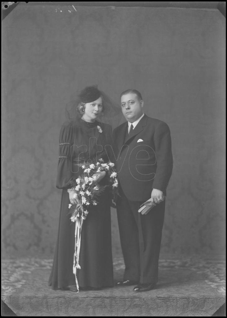 NOVIA VESTIDA DE NEGRO CON UN TOCADO Y UN RAMO, DE PIE JUNTO