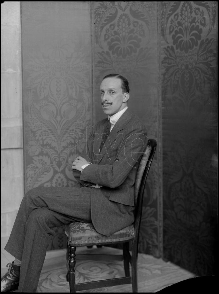 ALFONSO XIII SENTADO EN UNA SILLA CON LOS BRAZOS CRUZADOS