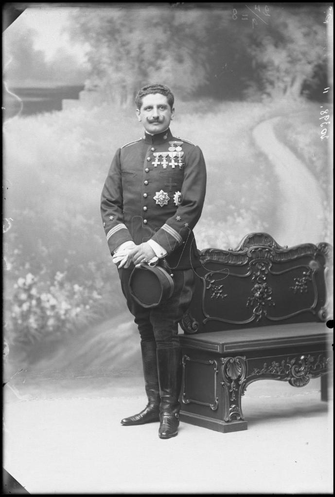 CAPITAN DE ARTILLERIA CONDECORADO, DE PIE JUNTO A UN BANCO