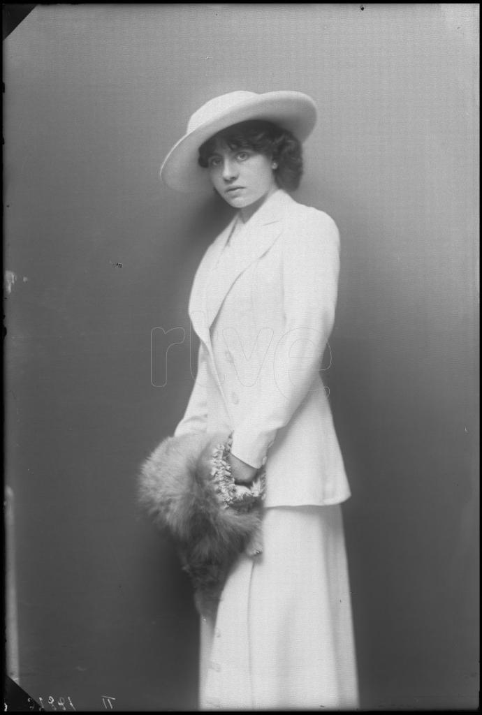 MIMI ESTAMPES CON UN TRAJE BLANCO, UN SOMBRERO Y UN MANGUITO